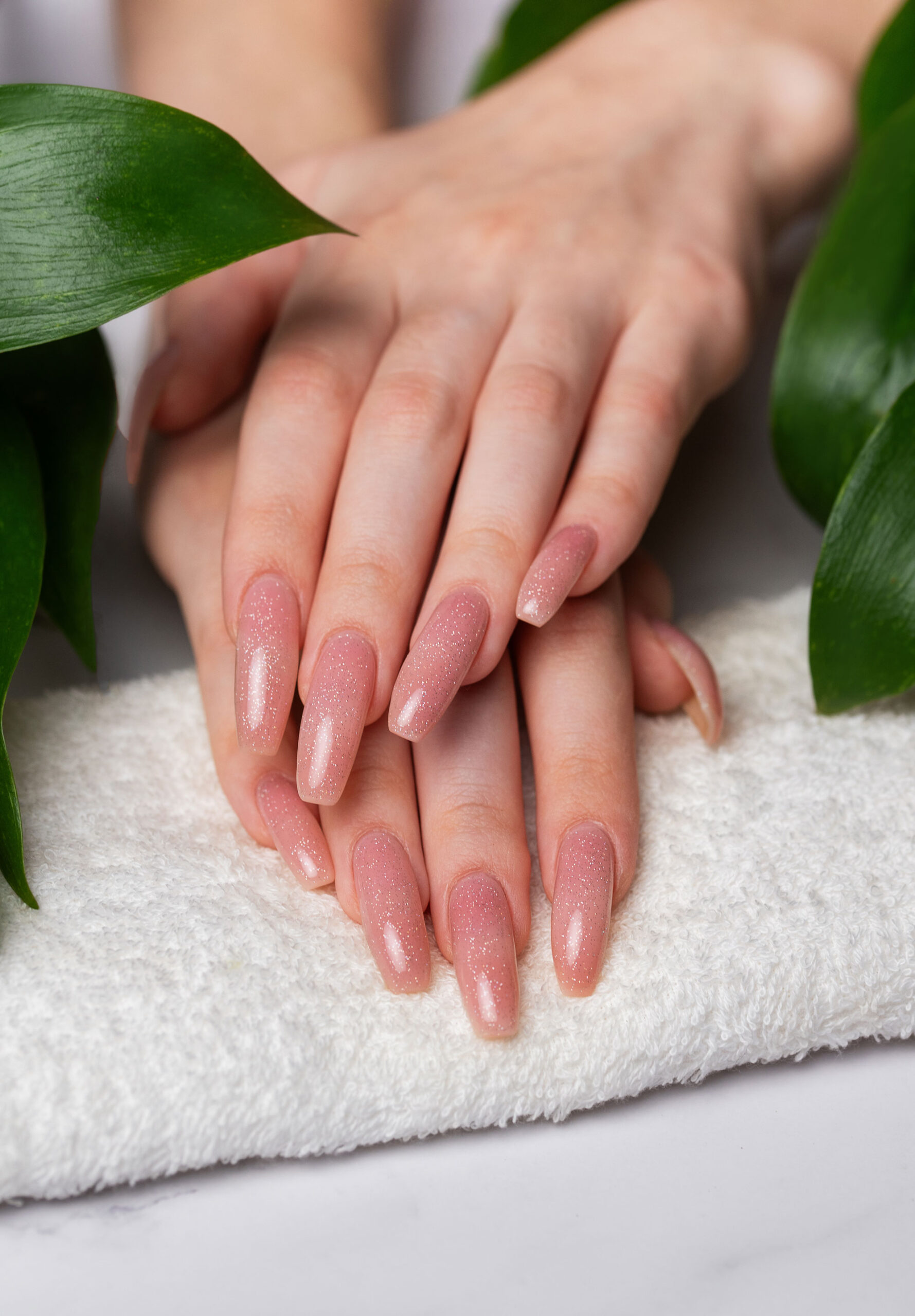 Soft pink gel manicure beautiful hands on towel with green leaves surrounding